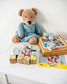 Bauklötze-Puzzle und gestrickter Teddybär mit Puppenkleid auf weißem Kindertisch