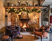 Two armchairs in front of open fireplace decorated with festive garland