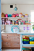 Colourful crockery on wall-mounted shelves above wooden cupboards in kitchen