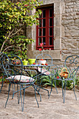 Ornate metal chairs and table outside window of stone house