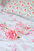 Artificial rose and string of beads on floral bedlinen