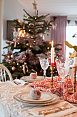 Christmas tree behind dining table set in classic style with sugar-coated apples on plates