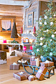 Verpackte Geschenke und ein Schlitten vor dem Weihnachtsbaum