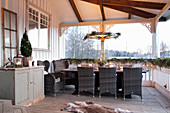 Dining table and faux-wicker chairs on rustic veranda with winter decorations