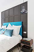 Bed with turquoise headboard against black panelled wall