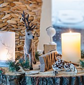Rustic Christmas arrangement of reindeer figurine, candle, lantern and pine cones on slice of tree trunk