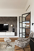Easy chair with matching footstool in elegant living room with open glass door and TV on floating cabinet