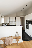 Wooden bench against counter in white fitted kitchen