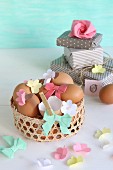 Ausgepustete Eier dekoriert mit Papierblumen und Papierschleife in Osterkörbchen