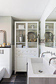 Old glass-fronted cabinet and twin sinks in white bathroom