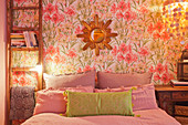 Ladder leant against floral wallpaper and used as bedside table in bedroom