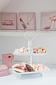 Pastel-coloured pastries on cake stand in front of feminine pictures