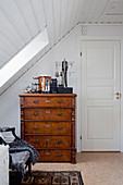 Jewellery on antique, wooden chest of drawers below sloping ceiling