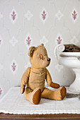 Old, patched teddy bear in front of vintage-style wallpaper