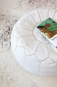 Book on white leather pouffe on white cowhide rug