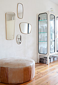 Various retro mirrors on wall above old leather pouffe