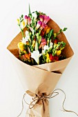 Bouquet of colourful freesias being wrapped in brown paper