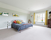 Colourful scatter cushions on metal bed against pale green bedroom wall