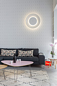 Circular lamp on wall above grey sofa and retro coffee tables