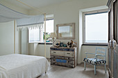 Shabby-chic chest of drawers in white and blue bedroom with sea view