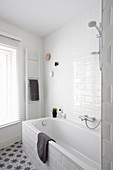 Weißes Badezimmer mit Badwanne, Handtuchtrockner und Fenster