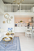 White couch, white dining table and kitchen below bedroom gallery in open-plan interior