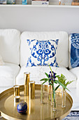 Glass vases and candles on round tray table in front of white couch with white and blue scatter cushions
