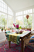 Runner and flowers on dining table with rattan armchairs and potted plants in conservatory