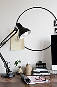 Black table lamp on desk and round black frame on wall used as pinboard