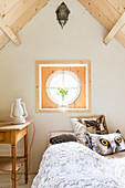 Cushions with animal motifs on bed below round window in gable end wall