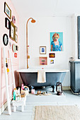 Grey, free-standing bathtub below pictures on pink wall