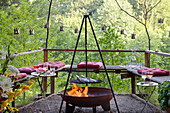 Candle lanterns hand-made from tin cans hung above benches and fire pit on natural terrace