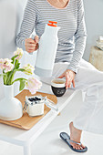 Woman with thermos flask of coffee, yoghurt with blueberries and vase of tulips on tray