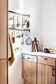 Utensils hung from hook rails in kitchen with wooden cabinets