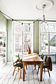 Dining table and chairs in front of large windows in dining room with green walls and white wooden floor