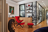 Red designer armchair with footstool in open-plan interior