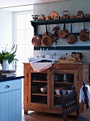 Copper pans on shelves above open-fronted wooden cabinet