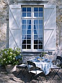 Gedeckter Gartentisch vor einem Sprossenfenster mit Fensterläden
