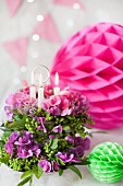 Flower arrangement with candles on cake stand and colourful honeycomb paper balls