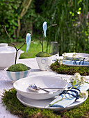 Gedeckter Tisch im Garten mit Moos, Zweigen und Vögelchen als Deko