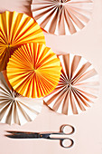 Scissors next to yellow and pink paper rosettes