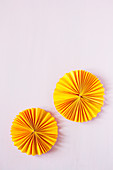Two sunny yellow paper rosettes on pink surface