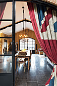 Union-flag-patterned curtains on open door with view of dining table in converted barn