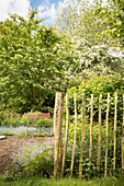 Blick in frühsommerlichen Garten mit Staketenzaun und Klappstühlen am Gartenbeet