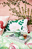 Tray with tea set and cushions on a bench in front of pink wall