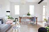 Grey sofa and old wooden table and chairs in open-plan interior with white walls
