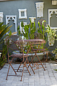 White picture frames on grey wall, foliage plants, table and chairs in courtyard