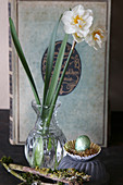 Narcissus in vintage vase and mossy branch in front of old book