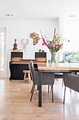 Bunter Esstisch mit grauen Stühlen, im Hintergrund Klavier mit Hocker in offenem Wohnraum