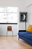 Blaues Polstersofa, Stehlampe und Stuhl vor Fenster im Wohnzimmer mit Parkettboden im Fischgrätmuster